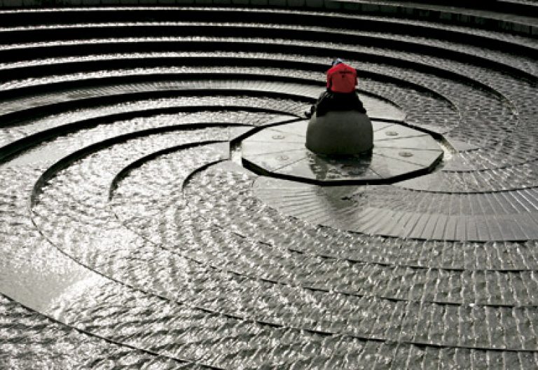 hombre sentado en medio de una fuente circular de piedra