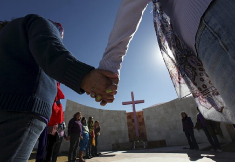 gente rezando cogida de la mano en círculo frente a una cruz