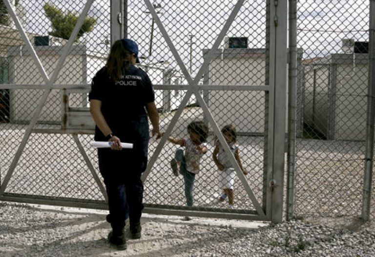 niñas iraquíes refugiadas hablando con una policía detrás de una valla en un centro de detención de inmigrantes en Grecia