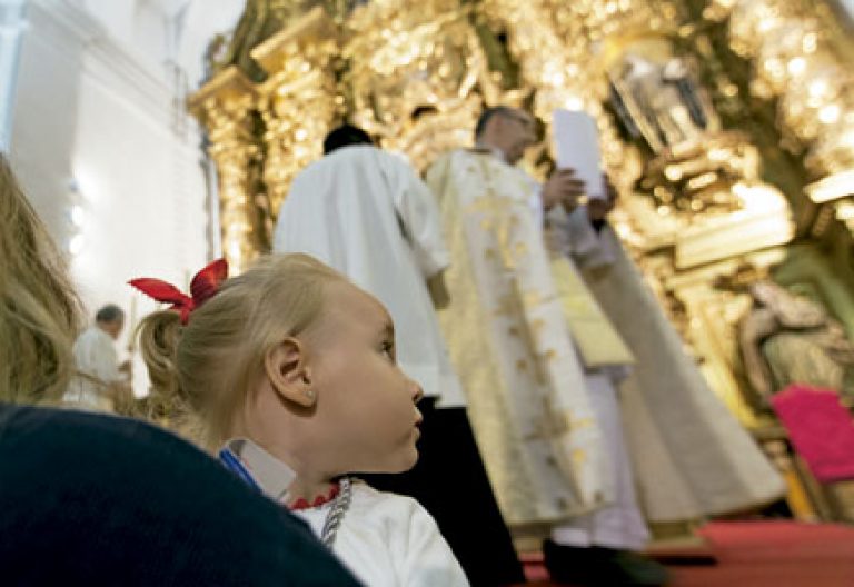 niña en brazos de su madre en una iglesia durante una misa con sacerdote