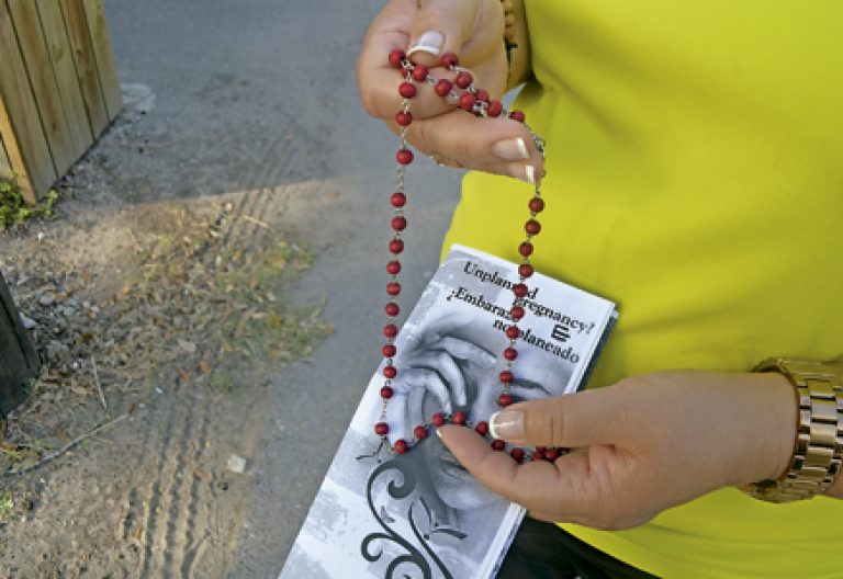 mujer con un folleto de información de un centro provida y un rosario
