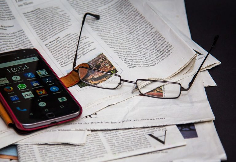 periódico en la mesa con unas gafas para leer y un teléfono móvil