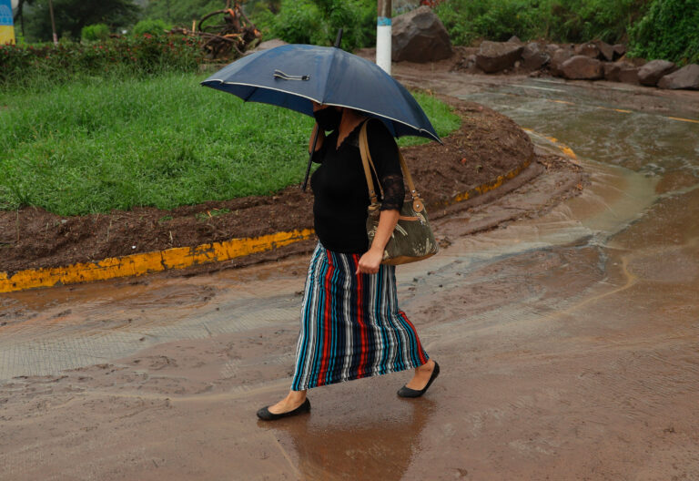 Mujer caminando bajo la lluvia en calle con barro
